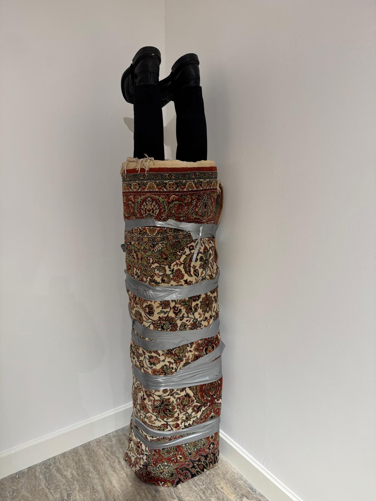 Silah Taciri, 2024. Makine halısı, pantolon, pabuçlar, bant vb. 190 x 40 x 40 cm.