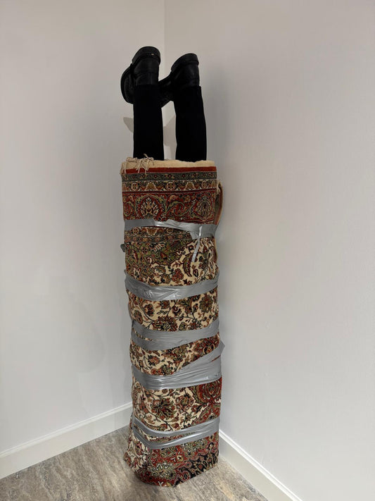 Silah Taciri, 2024. Makine halısı, pantolon, pabuçlar, bant vb. 190 x 40 x 40 cm.